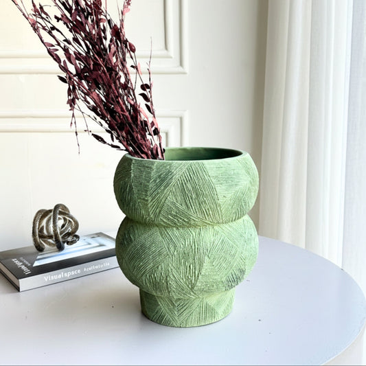 Green textured vase with dried purple flowers on a white surface