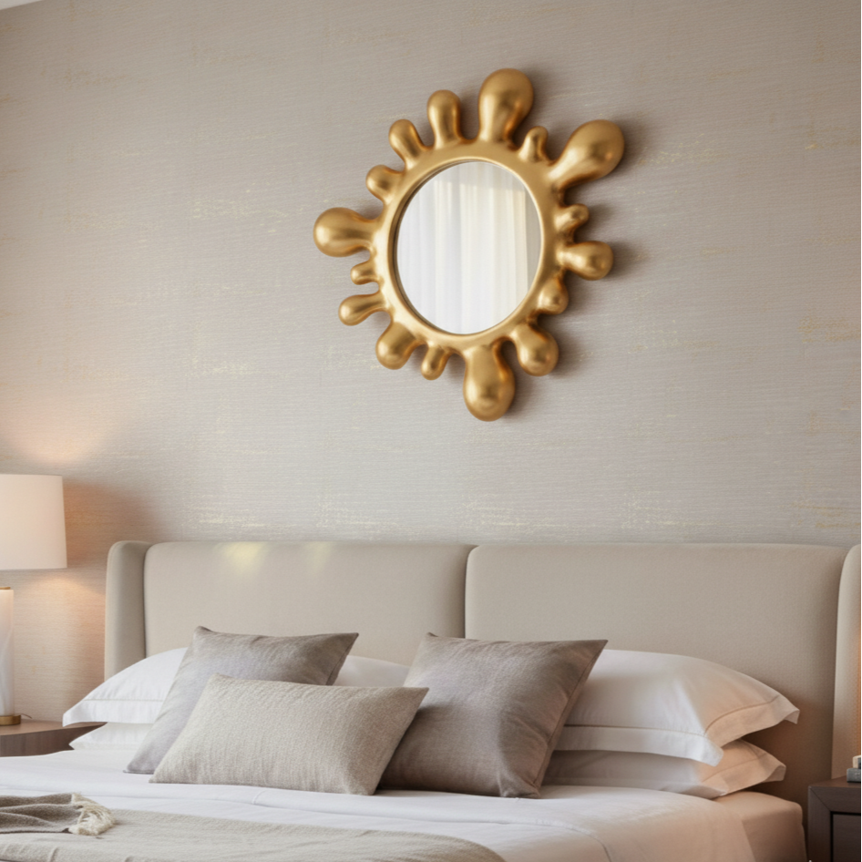 Gold sun-shaped mirror on a wall above a bed with pillows.