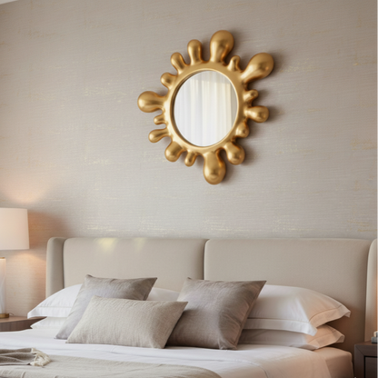 Gold sun-shaped mirror on a wall above a bed with pillows.