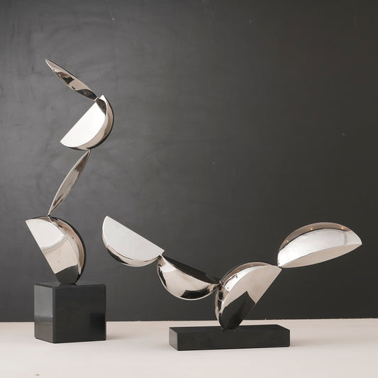 Abstract metallic sculpture on a black base against a gray background