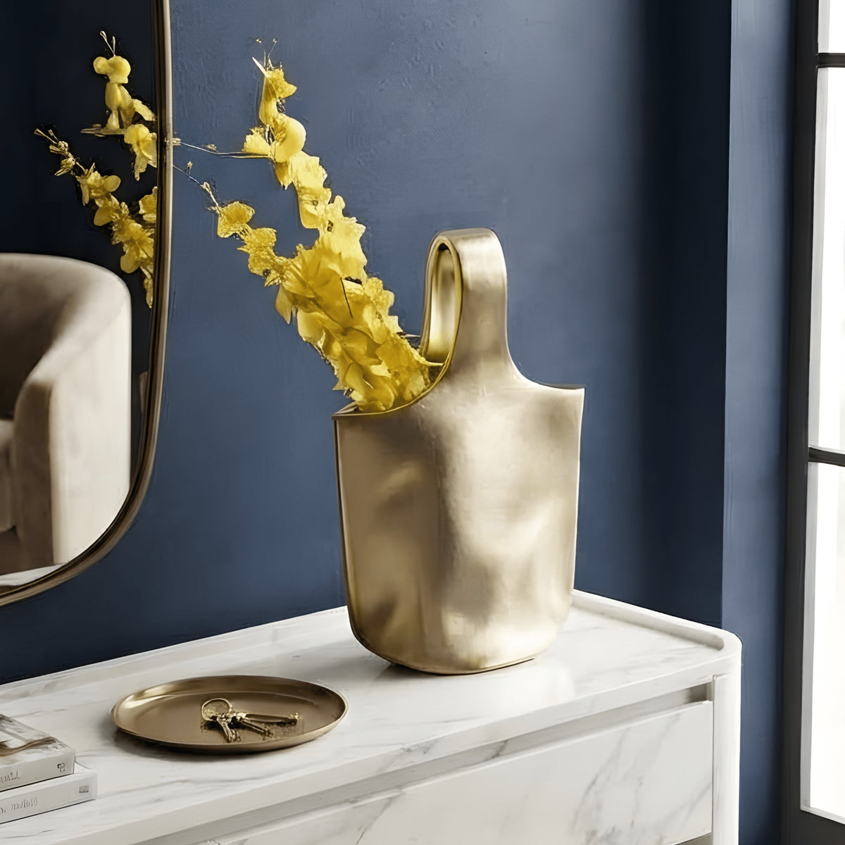 Aurea sculptural gold ceramic vase styled on an entryway console against a deep blue wall