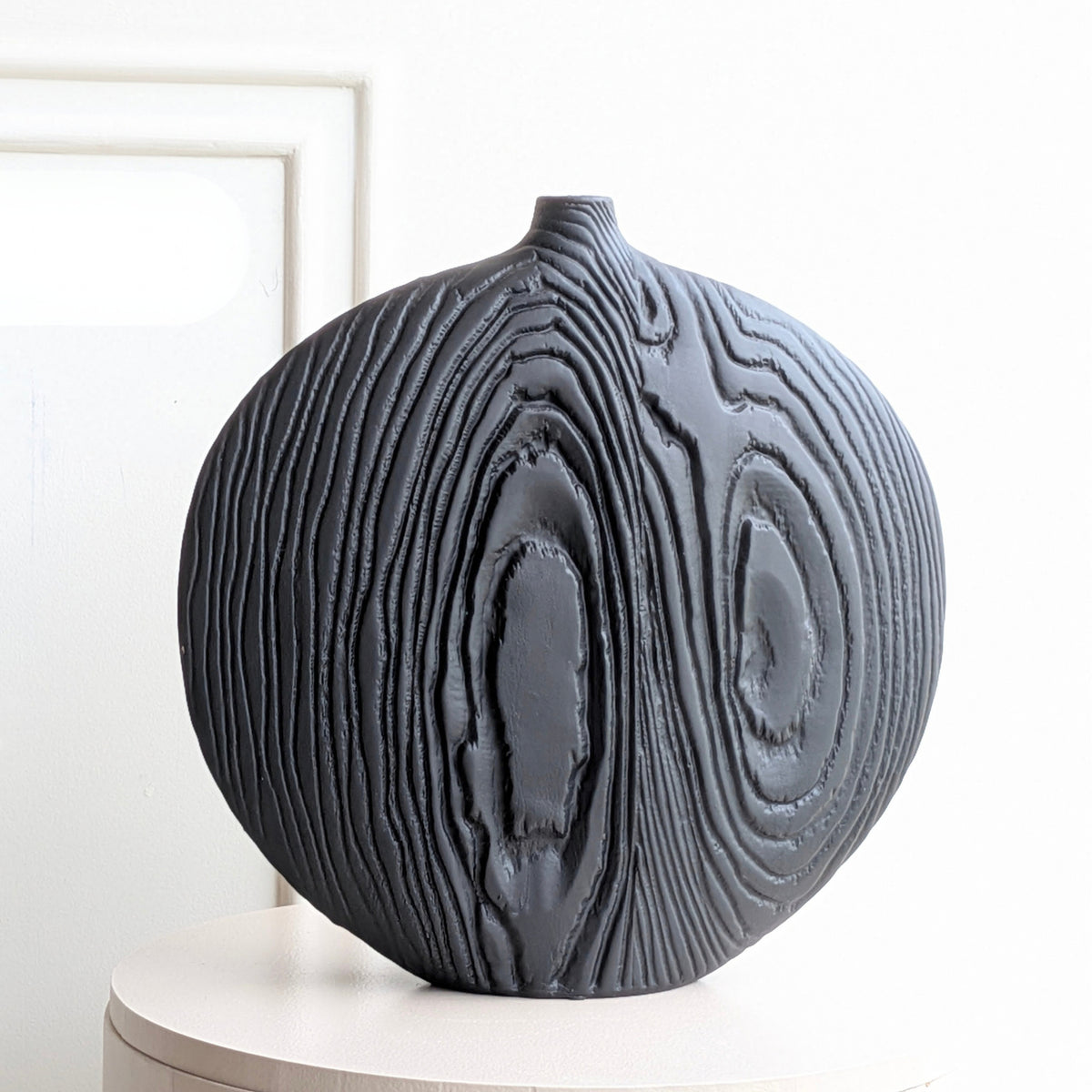 Front product view of large round black ceramic table vase with carved concentric woodgrain-inspired relief