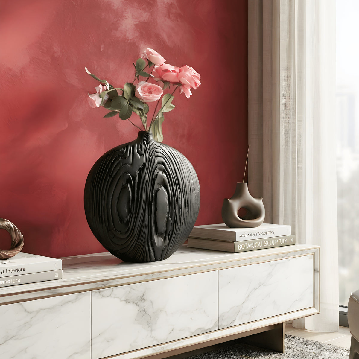 Black sculptural ceramic vase with pink roses on marble console against a red feature wall