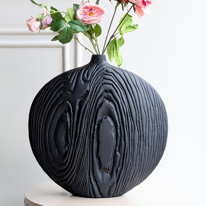 Close detail of dark charcoal ceramic vase with deeply carved concentric texture and rose arrangement