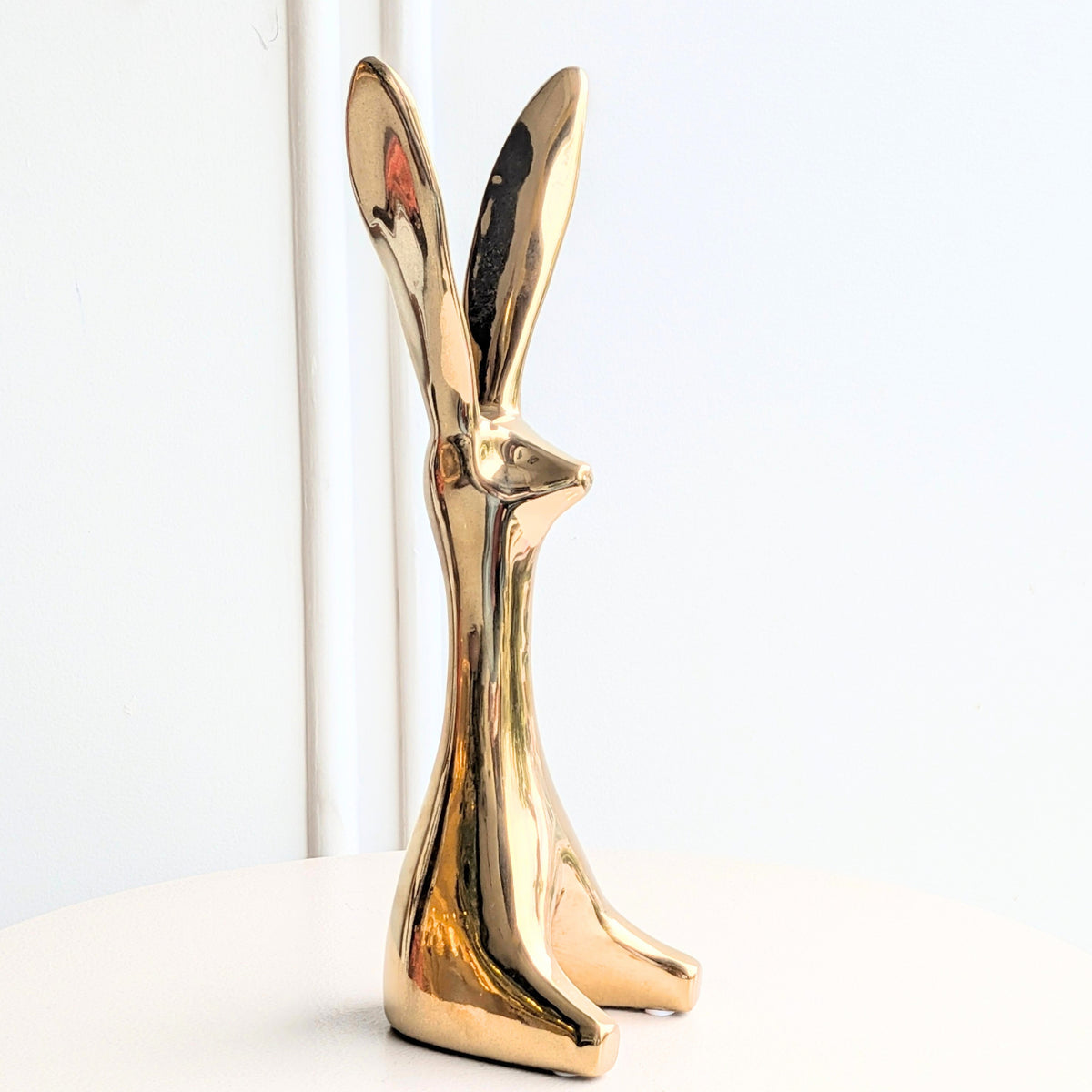 Large gold ceramic rabbit showpiece for console styling beside decor books and a vase