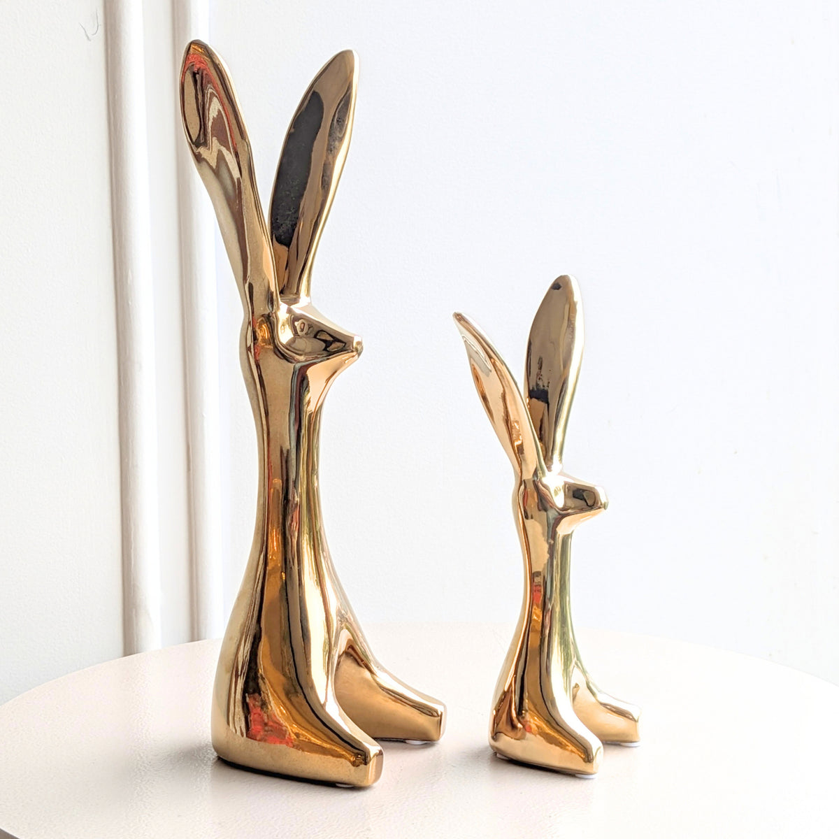 Hareloom polished gold ceramic hare sculptures in two sizes shown together on a display table