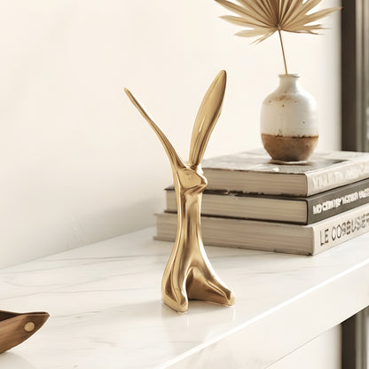 Small gold ceramic rabbit sculpture shown on a tabletop with elongated asymmetrical ears