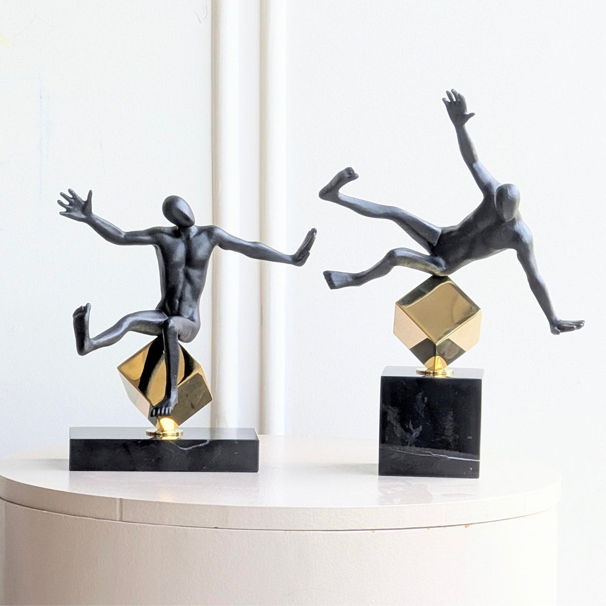 Front view of Kinesis black metal balancing human figurines with gold geometric forms