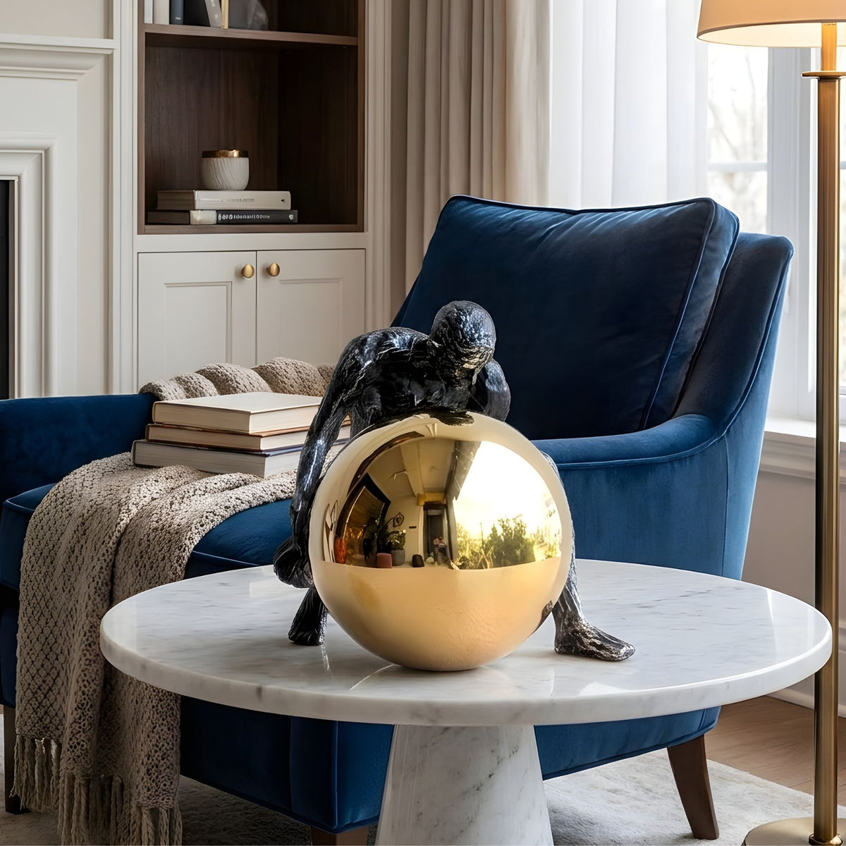 Strive dark metal human figure and gold sphere on a marble side table beside a blue armchair