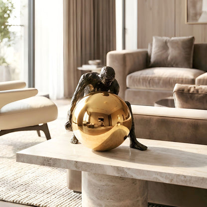 Strive gold sphere sculpture with kneeling metal human figure, side profile