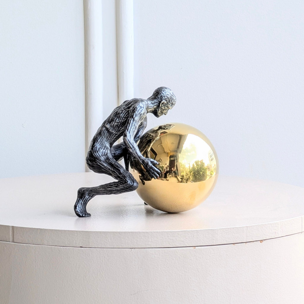 Strive metal human figurine pushing a polished gold sphere, product front view