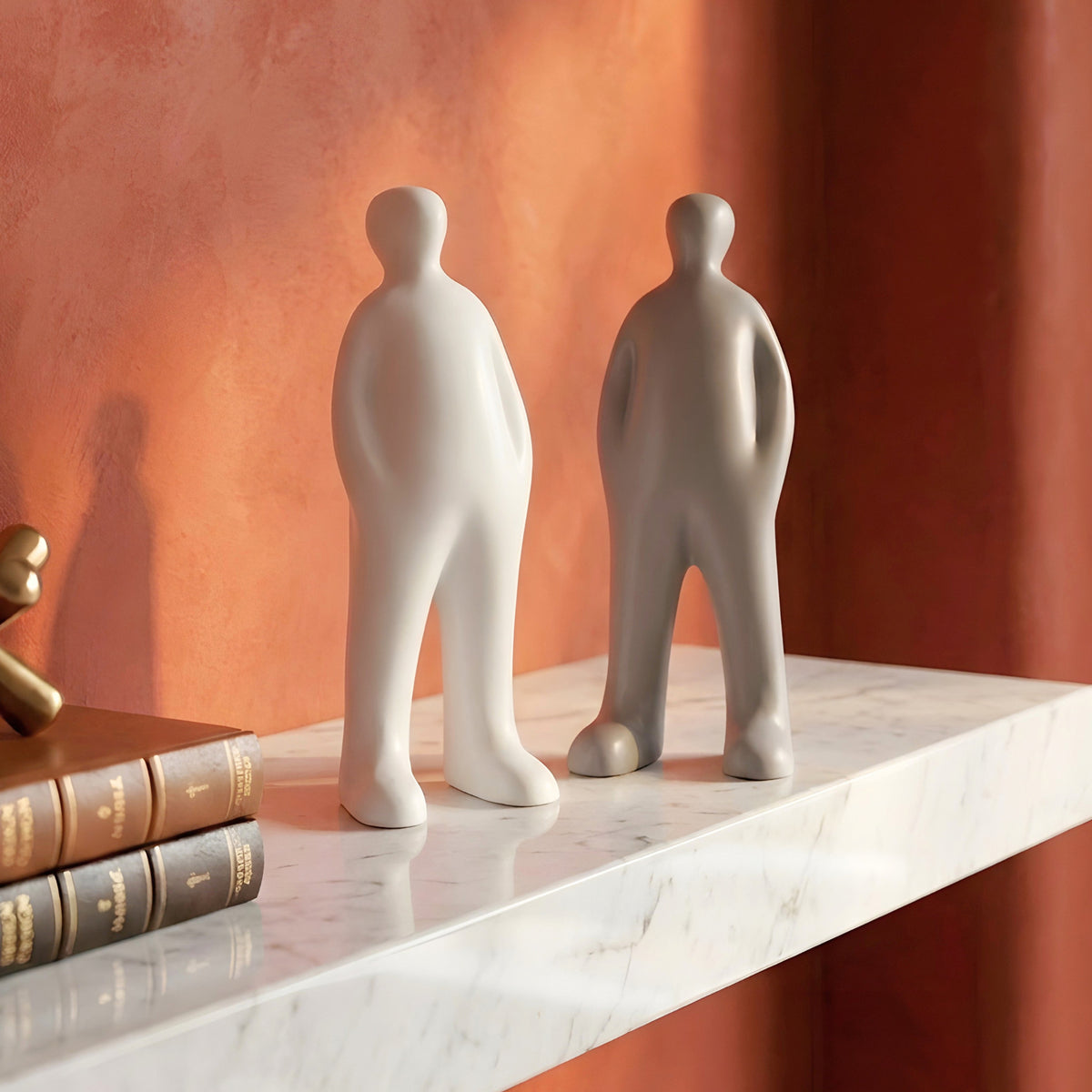 Off Duty Grey and White resin human figurines on a marble shelf against a terracotta wall